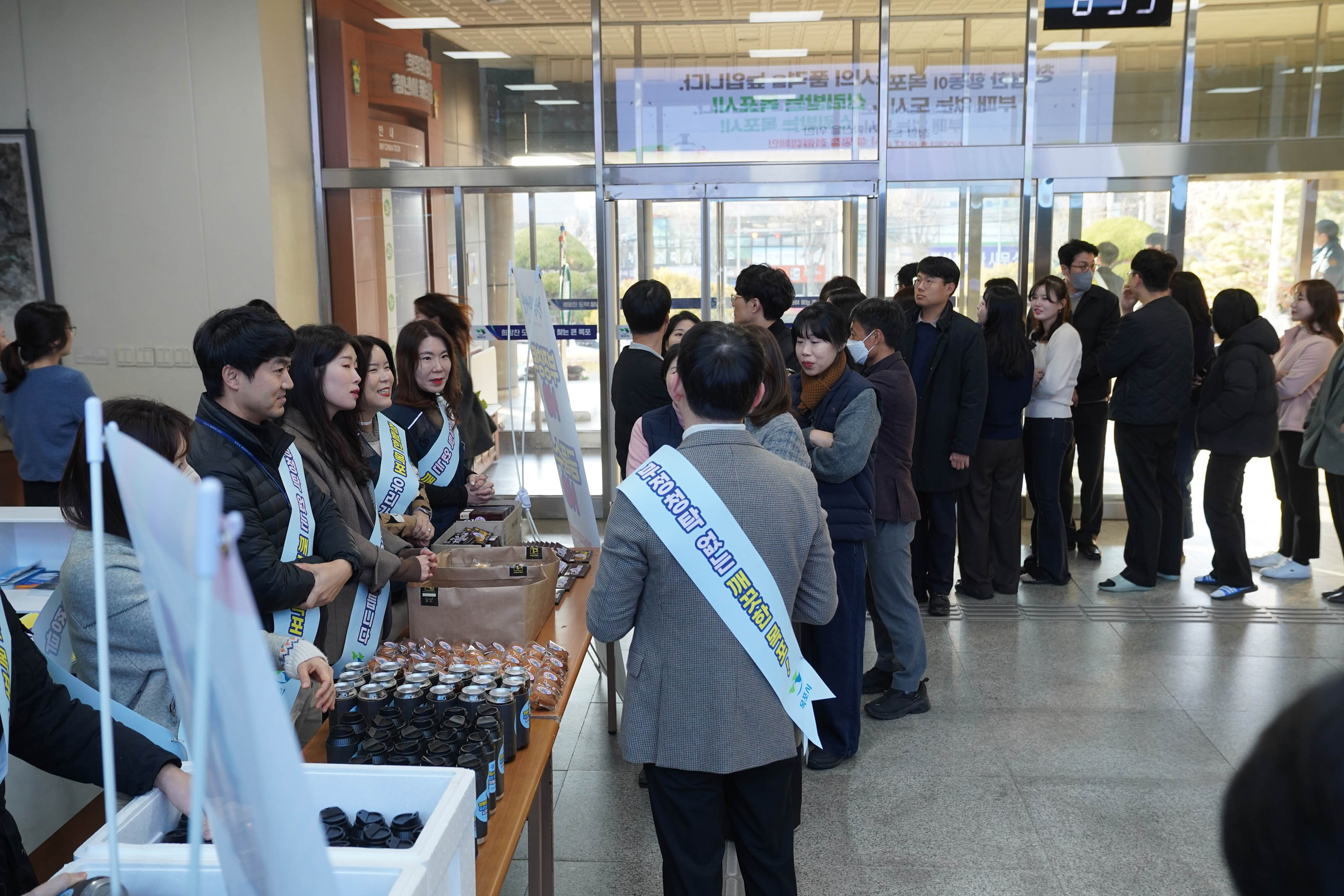 '설 명절 청렴캠페인' 행사에서 청렴 캠페인 관련 슬리브를 착용 직원들보이며 테이블에는 텀블러와 상품들이 진열되어있다. 10여명의 참석자들이 줄을 서서 기다리고 있다 .