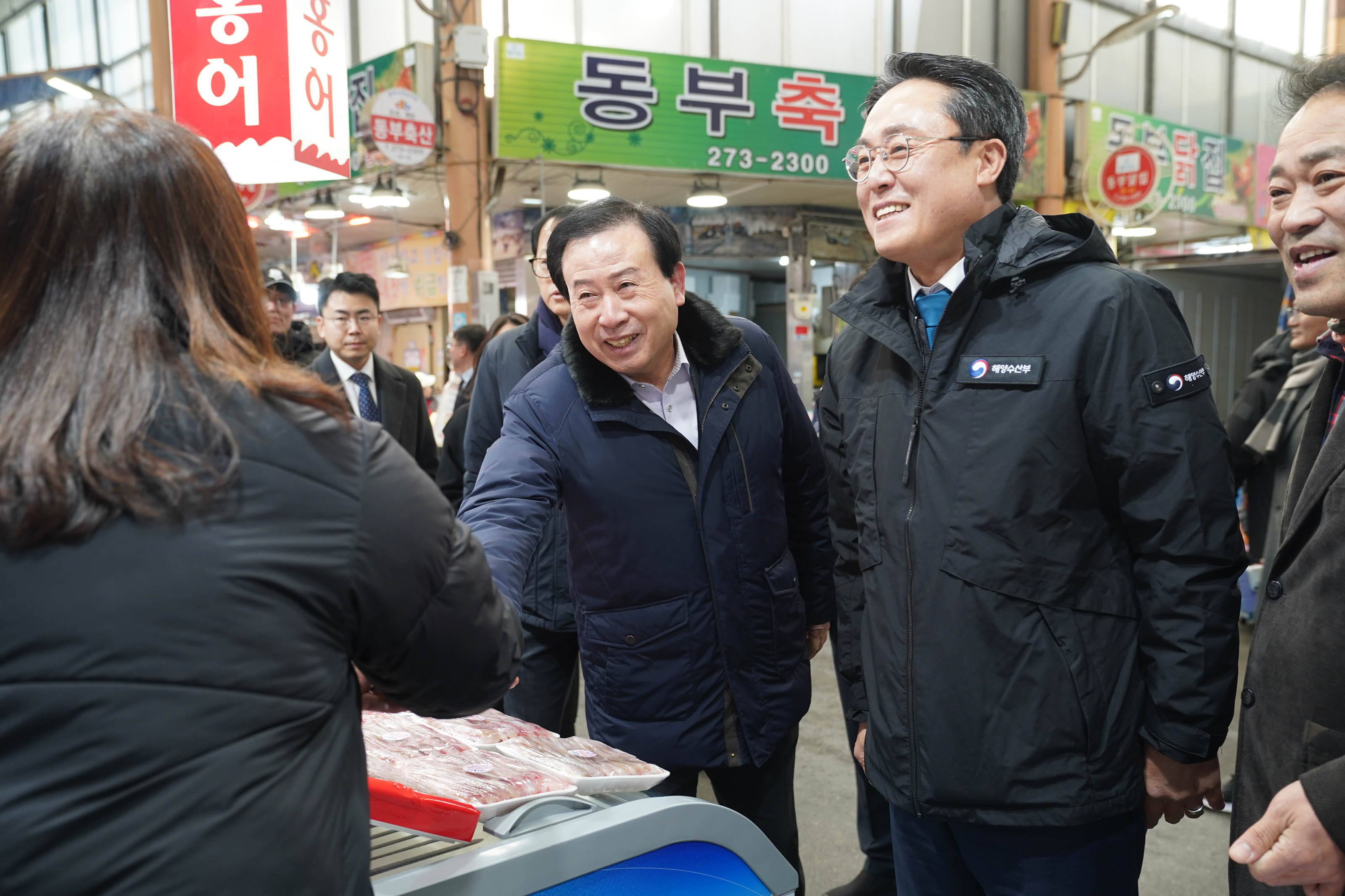 전통시장에서 박홍률 목포시장이 웃으며 여성 상인과 악수하고 있으며, 강도형 해수부장관과 여러 관계자들이 함께 상황을 지켜보고 있다.