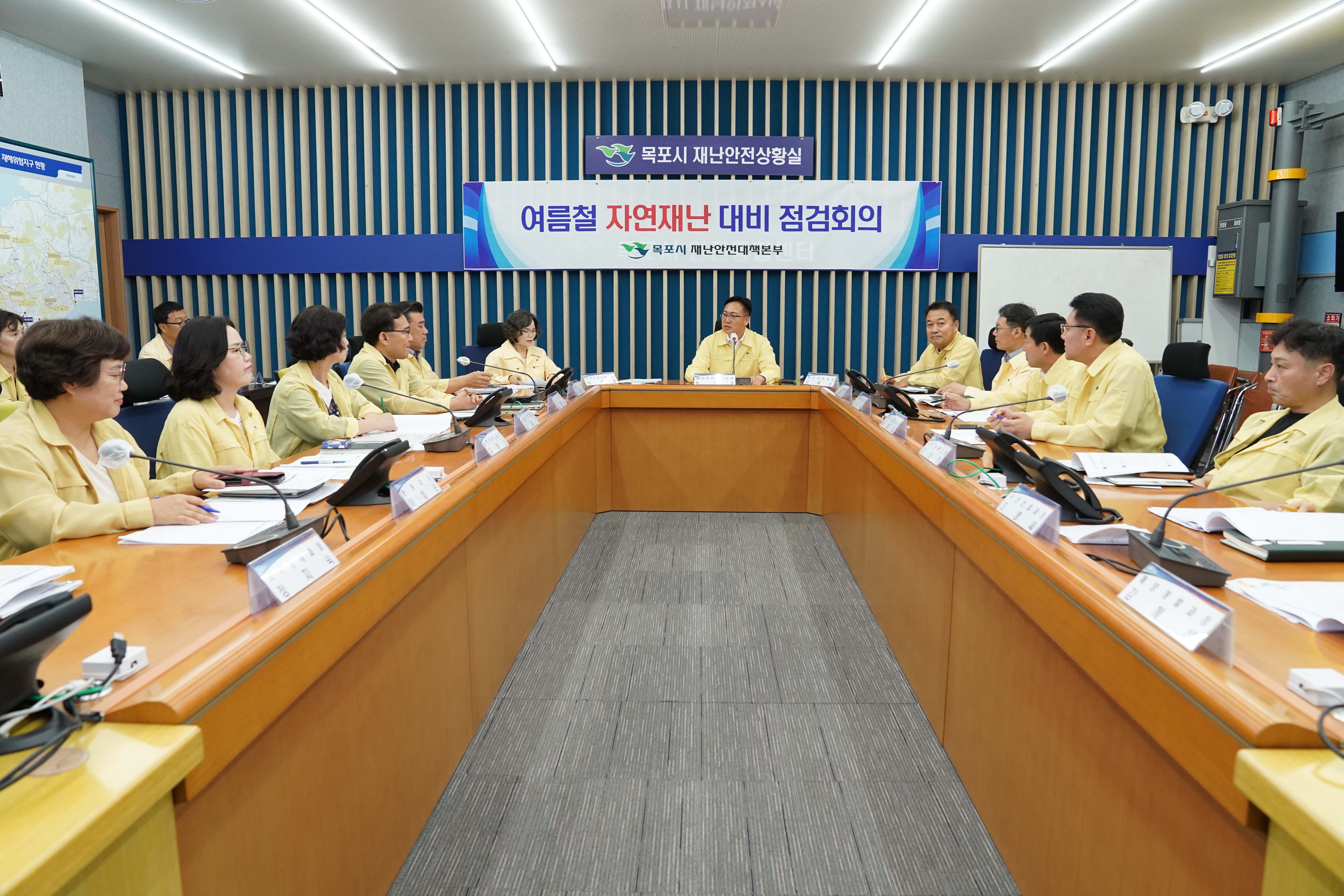 목포시 재난안전상황실 회의실 전체 전경. '여름철 자연재난 대비 점검회의' 현수막 아래로 노란색 민방위복을 입은 다수의 공직자들이 'U'자형 테이블에 앉아 회의에 집중하고 있습니다.