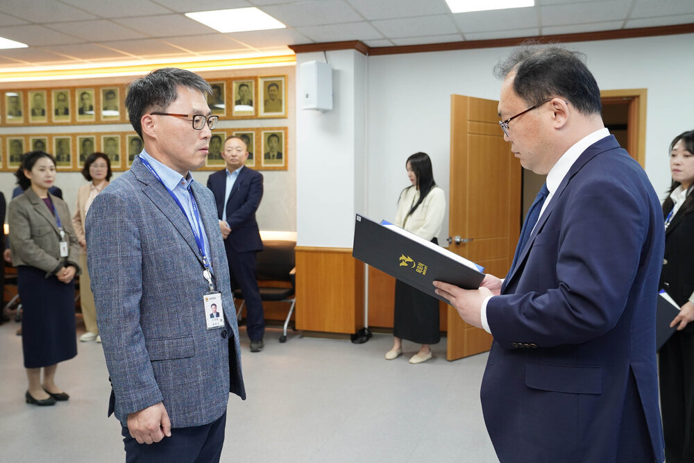 수시인사 임용장 수여식에서 정장을 입은 남성이 회색 재킷을 입은 남성 직원에게 임용장을 전달하는 모습