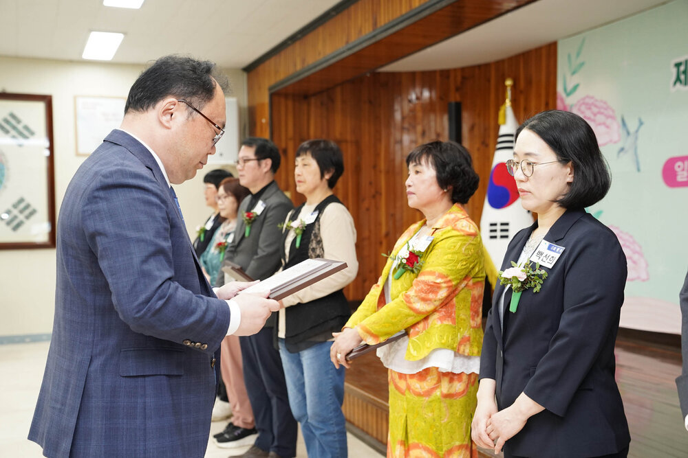 정장을 입고 안경을 낀 남성이 검은색 7부 자켓을 입고 있는 백선희에게 패를 수여하고 있다