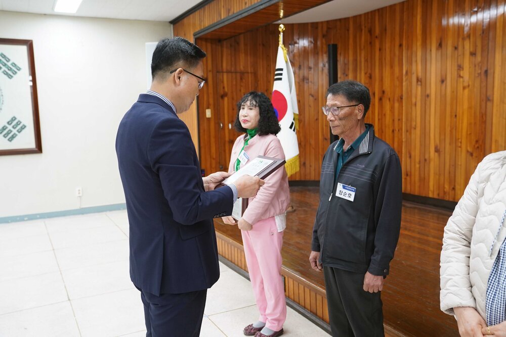 4월 정례조회에 정장을 입고 안경을 낀 남성이 어두운색 바지와 점퍼를 입은 장순호에게 패를 수여하고 있다