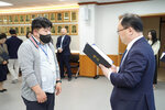 수시인사 임용장 수여식에서 정장을 입은 남성이 회색 점퍼를 입고 마스크를 착용한 남성 직원에게 임용장을 전달하는 모습